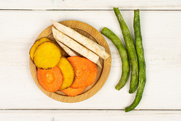 Lot of whole dry vegetable chip on bamboo coaster flatlay on white wood