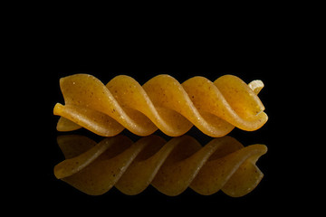 One whole dry brown wholegrain fusilli isolated on black glass