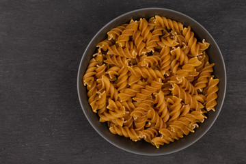 Lot of whole dry brown wholegrain fusilli in gray ceramic bowl flatlay on grey stone
