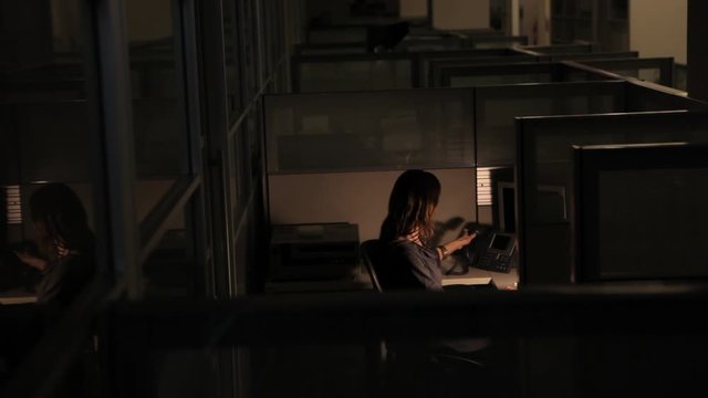 Happy businesswoman working late in office cubicle answering phone