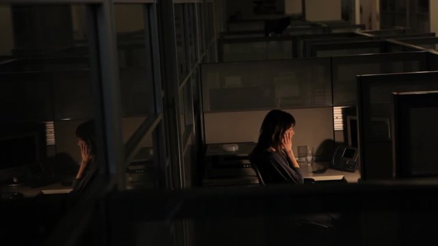 Stressed and fatigued businesswoman working late in office cubicle rubbing her tired eyes