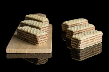 Group of six whole crispy beige hazelnut wafer cookie on small wooden cutting board isolated on black glass
