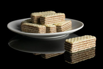Lot of whole crispy beige hazelnut wafer cookie on white ceramic plate isolated on black glass