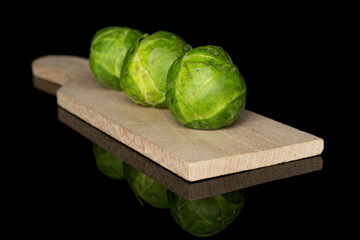 Group of three whole fresh green brussels sprout on wooden cutting board isolated on black glass