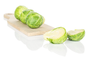 Group of three whole two halves of fresh green brussels sprout on wooden cutting board isolated on white background