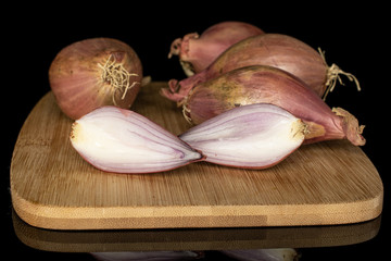 Group of four whole two halves of fresh brown shallot on bamboo cutting board isolated on black glass