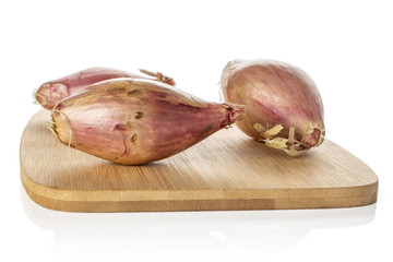 Group of three whole fresh brown shallot on bamboo cutting board isolated on white background