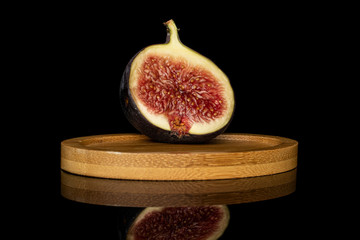 One half of sweet purple fig on round bamboo coaster isolated on black glass