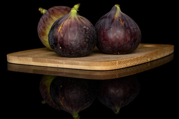 Group of three whole sweet purple fig on bamboo cutting board isolated on black glass