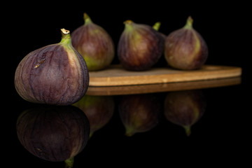 Group of four whole sweet purple fig on bamboo cutting board isolated on black glass