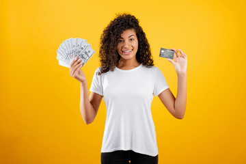 young african black woman with dollars money and credit card in hand isolated over yellow