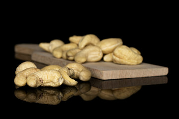 Lot of whole brown nut cashew five in focus on wooden cutting board isolated on black glass