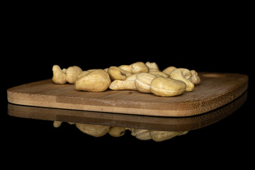 Lot of whole brown nut cashew on bamboo cutting board isolated on black glass