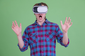 Young hipster man looking shocked while using virtual reality headset