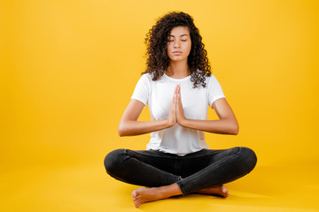 relaxed black woman meditating in yoga pose isolated over yellow