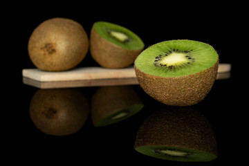Group of one whole two halves of exotic brown kiwi on wooden cutting board isolated on black glass