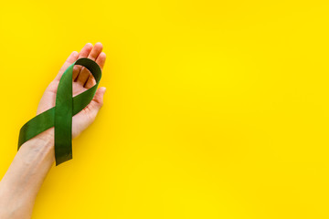 Jade ribbon in hands as symbol of disease control on yellow background top view space for text