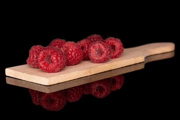 Lot of whole fresh red raspberry on wooden cutting board isolated on black glass