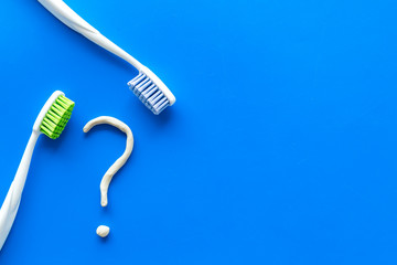 Dental problems concept. Question mark drawn with toothpaste near toothbrush on blue background top view