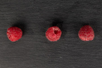 Group of three whole fresh red raspberry flatlay on grey stone