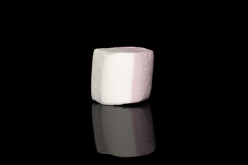 One whole sweet pastel marshmallow isolated on black glass