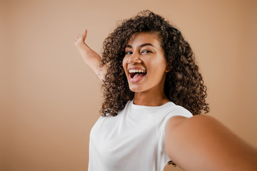 lovely happy black young woman making selfie isolated over brown