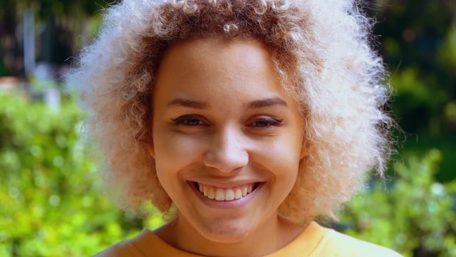 close up face young laughing girl african american woman looking camera and smiling outdoors background