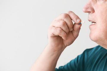 Elderly man taking medicine on light background, closeup