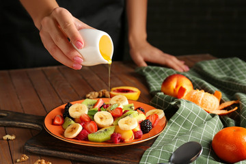 Woman preparing tasty fruit salad at table, closeup