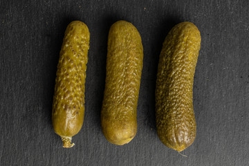 Group of three whole sour green pickle flatlay on grey stone