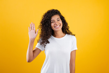 black woman smiling waving hello with hand isolated over yellow © Anastasia