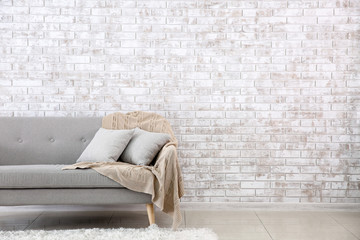 Comfortable sofa near brick wall in room