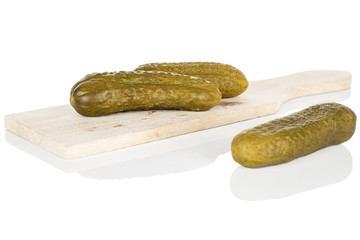 Group of three whole sour green pickle front focus on wooden cutting board isolated on white background