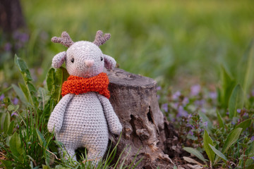 Beautiful handmade soft toy fawn. Outdoor photography, grass and a small stump.