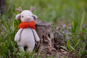 Beautiful handmade soft toy fawn. Outdoor photography, grass and a small stump.