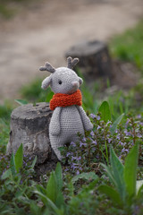 Beautiful handmade soft toy fawn. Outdoor photography, grass and a small stump.