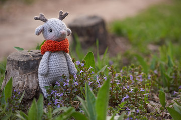 Beautiful handmade soft toy fawn. Outdoor photography, grass and a small stump.