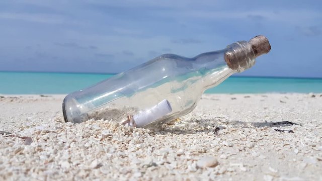 A glass bottle sealed with a cork  and a rolled up paper inside rests on clean white coral sand on a tropical island in the Caribbean
