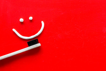 Teeth health concept. Smile drawn with toothpaste near toothbrushes on red background top view space for text
