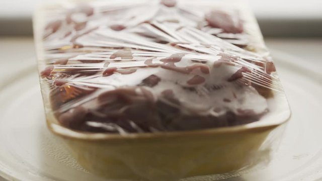Fresh raw сhicken offal in food tray with plastic wrap rotating in microwave.