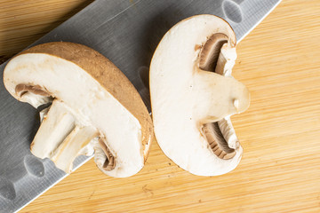 Group of two whole fresh brown mushroom champignon with steel knife flatlay on light wood