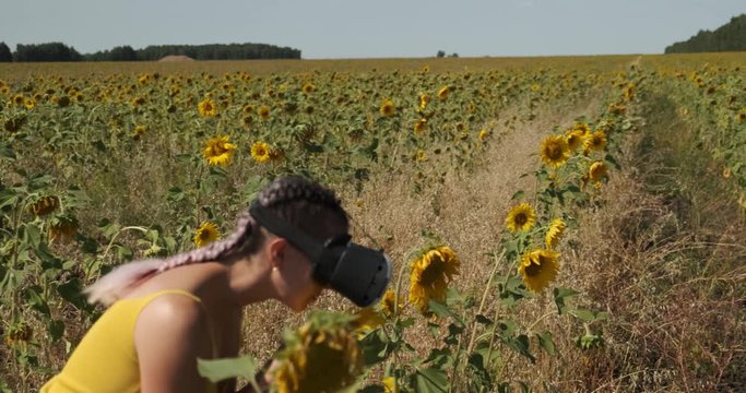 In an endless sunflower field, girl walks in virtual reality glasses, sunflowers, runs around field, enjoys playing outdoors, earns experience, helmet, is surprised by augmented reality, 3D technology