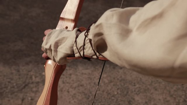 archery. man in gray linen suit inserts arrows into brown wooden bow, close-up, slow motion