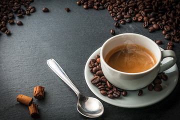 A cup of coffee on blue stone table with a spoon, cinnamon sticks and some fresh roasted coffee...