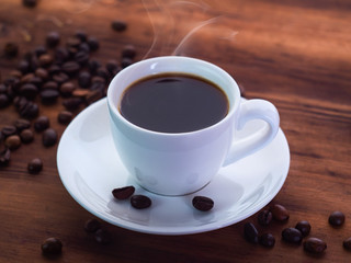 Coffee cup with espresso and coffee beans pilled on brown table, close up view. Texture of brown wooden table. Selective soft focus. Blurred background