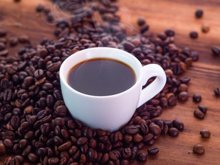 Coffee beans pilled round white coffee cup full of aromatic espresso, close up view. Texture of wooden desk. Art composition. Selective soft focus. Blurred background