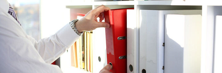 Male arms pick red file folder from office book shelf