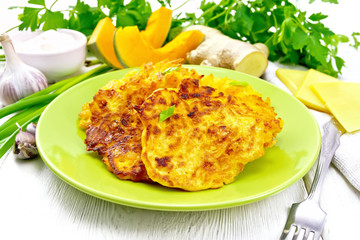 Pancakes of pumpkin with cheese in green plate on board