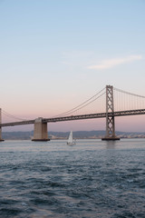 Sailboat under the bay bridge at dusk