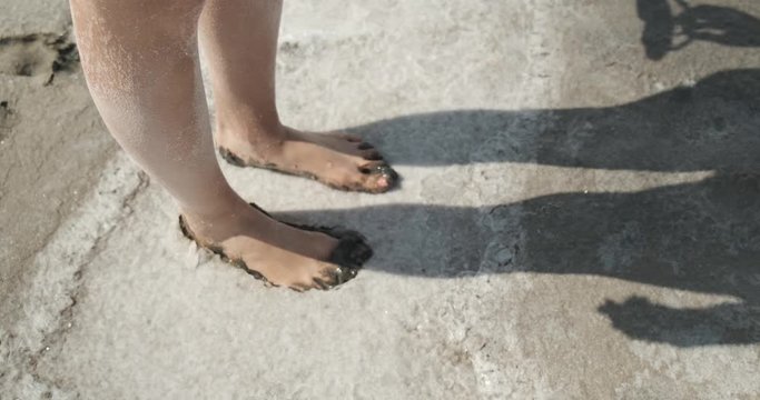 Close-up of slender female legs covered with healing mud, girl takes step forward, stops in layer of wet earth with salt, leaves traces, goes on, salt resort, outdoor recreation, hot summer weather
